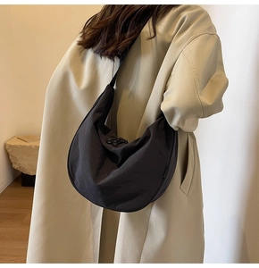 Close-up of minimalist black nylon crescent bag worn over a beige trench coat