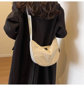 Detail view of cream nylon crescent bag with wrinkled texture on a black coat