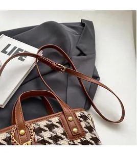 Detailed close-up of brown leather and houndstooth bucket bag with gold chain charm