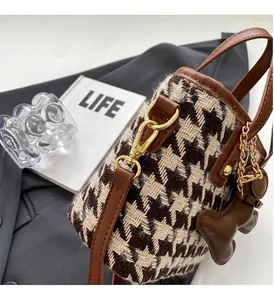 Detail of houndstooth bucket bag with brown leather trim and golden metal hardware