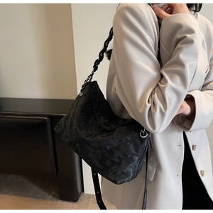 Detail of black quilted leather shoulder bag with silver chain strap and pleated texture