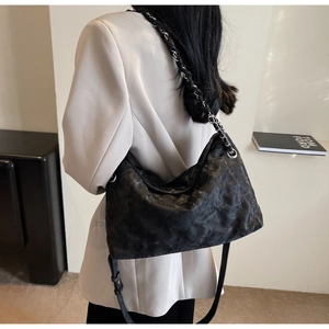 Detail of black quilted hobo bag featuring chain strap on a blazer-clad model