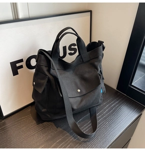 Detail of black canvas tote bag showing wide shoulder strap and metal snap pocket