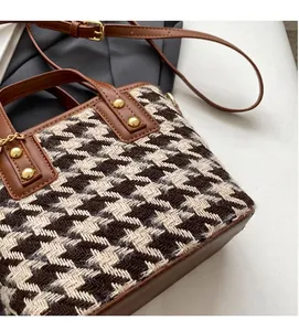 Detail of houndstooth wool fabric and brown leather strap on women's bucket bag