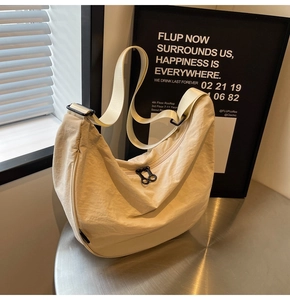Close-up of beige nylon crescent bag featuring double zippers and a wide shoulder strap