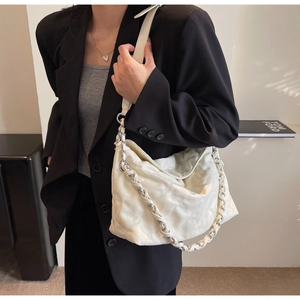 Detail of white quilted bag featuring a silver metal chain and leather woven strap