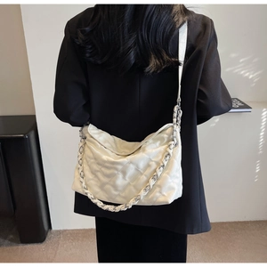 Detail of white quilted crossbody bag with leather chain strap on model with black blazer