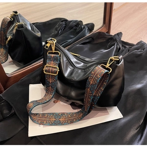 Close-up of black leather dumpling bag with bohemian ethnic patterned wide shoulder strap