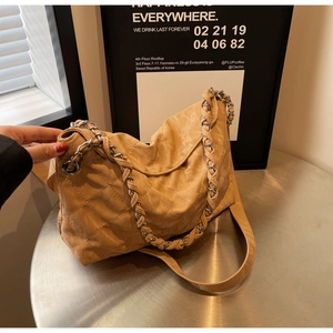 Detail of light brown quilted hobo bag with silver chain strap on metallic surface