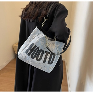 Detail view of denim canvas tote with paisley pattern and chain strap on shoulder