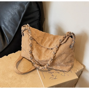 Detail of khaki quilted pillow bag with silver chain strap on a textured stone surface