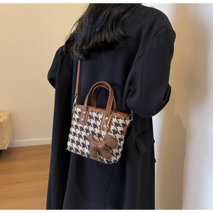 Detail van de houndstooth bucket bag met lederen riem en schattige dierenhanger