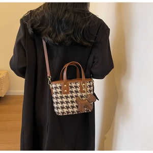 Detail van houndstooth crossbodytas met leren handvatten en hondenhanger-accessoire
