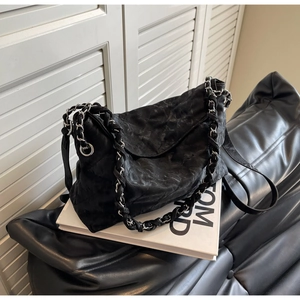 Detail of a black quilted leather shoulder bag with a woven chain strap in a home setting