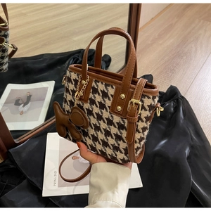 Detail van de kleine handtas met houndstooth-patroon, bruine leren bies en een hondenhanger