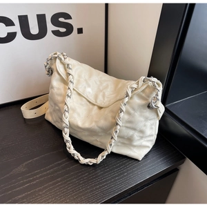 Detail view of a quilted cream shoulder bag with a metal chain strap on a black surface