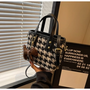 Detail van pied-de-poule bucket bag met bruine puppy-hanger en leren schouderband