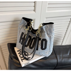 Detail of blue paisley denim tote bag with black letter patch and chain leather strap
