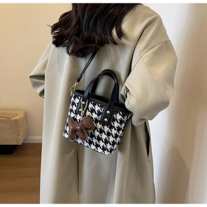 Detail van tweed houndstooth crossbodytas met hondenhanger en goudkleurig metaal