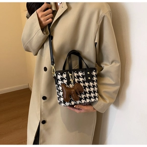 Detail van gebreide pied-de-poule tas met leren bies en bruine hondenhanger op model