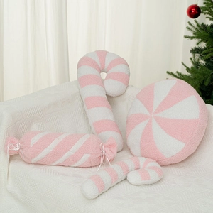 Pink and white striped plush Christmas candy pillows set on a soft white sofa