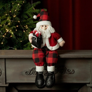 Babbo Natale di peluche seduto con cappello a quadri rossi sulla mensola del camino