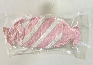 Détail d'un coussin en peluche rayé rose et blanc en forme de bonbon emballé sous vide