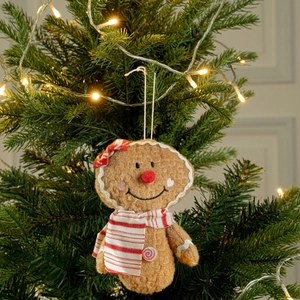 Gingerbread man plush ornament with striped bow hanging on a lit Christmas tree