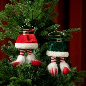 Détail de jambes d'elfe de Noël en tricot suspendues sur un sapin vert et fond rouge