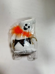 Knitted Halloween ghost doll with orange feathers and black banner in macro detail view