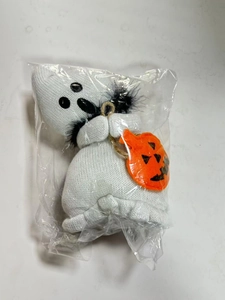 Detailed view of a white knitted Halloween ghost doll with a pumpkin bag in clear packaging