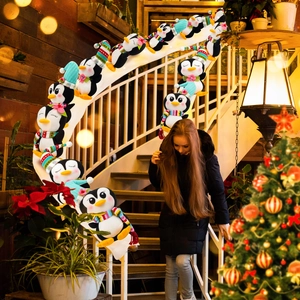 Trois pingouins de Noël en peluche sur une rampe d'escalier avec décorations festives