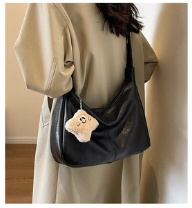 Detail of black faux leather tote with plush star charm on woman in beige trench coat