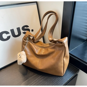 Detail of a brown leather shoulder bag with a cute white plush bear charm on a wood surface