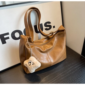 Close-up of brown vintage leather dumpling bag with plush smiley pendant and adjustable strap