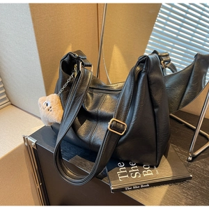 Close-up of a large black faux leather hobo bag with a plush charm on a book
