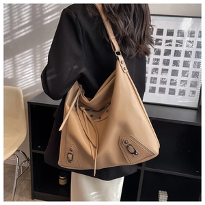 Detail of khaki leather tote with tassels and metallic rivets worn by a model