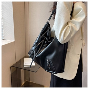 Macro detail of black leather tote bag featuring long tassels and metallic stud buckle accents