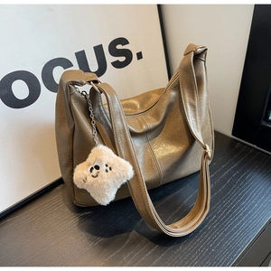 Close-up of brown soft leather shoulder bag with plush pendant and zip closure