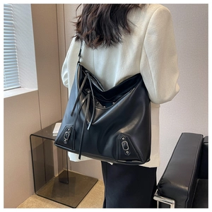 Detail of black large tote bag with long tassels and metal buckles on white blazer