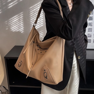 Large khaki tote bag with studs and tassels shown on a model in a minimalist setting
