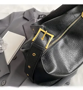Détail du sac en cuir noir à texture litchi avec ferrures dorées et bandoulière large