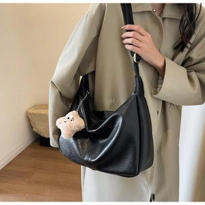 Detail of black dumpling bag with lychee texture and cute plush bear charm decoration