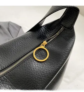 Détail d'un sac en cuir grainé noir avec une tirette de fermeture éclair circulaire dorée