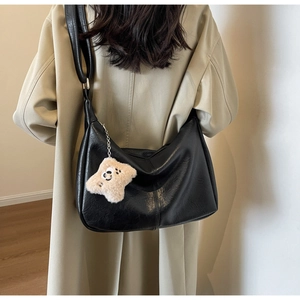 Detail of a large black vintage hobo bag with a star plush charm on a beige trench coat