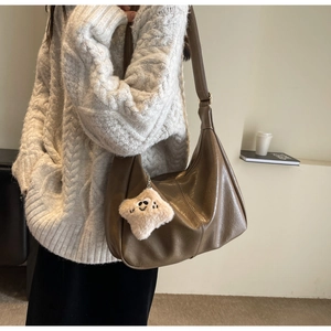 Detail of dark brown leather hobo bag with a plush star charm on a beige sweater