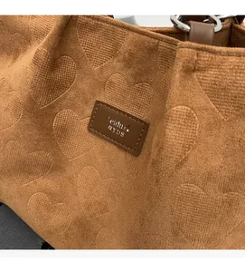 Detail view of brown matte suede tote featuring embossed heart patterns and leather logo