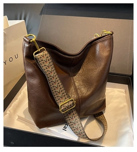 Detail of vintage brown leather bucket bag with colorful woven wide shoulder strap