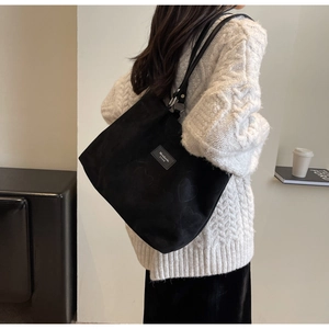 Detail of black tote bag featuring subtle heart pattern and stylish leather logo patch
