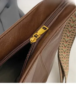Close-up of golden metal zipper and woven strap on vintage brown leather tote bag
